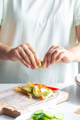 Woman preparing spring rolls in rice paper on kitchen table.