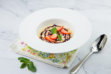 porridge with strawberries, mint and berry jam in a white plate, side view
