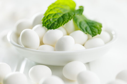 Mint candies in bowl. Menthol bonbons and mint leaves on white table.