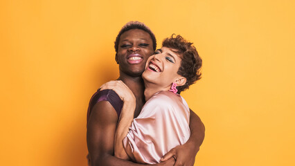 Stylish trans men in make up and fashion clothes embracing and smiling on yellow - obrazy, fototapety, plakaty