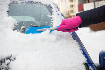 Hand of woman using brush and remove snow from car and windscreen
