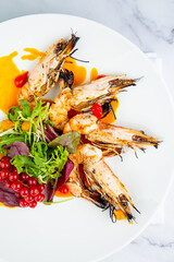 cooked shrimp with herbs and berries on a white plate, top view