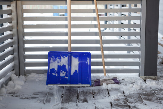 Snow shovel and brush on a snow-covered veranda of a wooden house