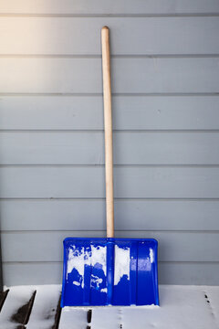 Snow plastic shovel leaning against the wooden wall of the house