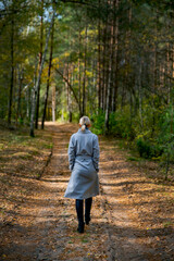 Girl walking in the woods on a path, photographed from the back. Autumn coloured trees can be seen, elegant looking woman walking with confidence as a main subject