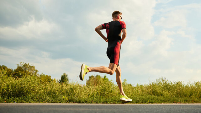 Dynamic image of competitive man in sportswear, athlete training outdoors on summer day, running. Marathon. Concept of professional sport, triathlon preparation, competition, athleticism