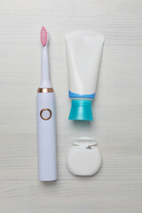 Electric toothbrushes, dental floss and tube on white wooden background, top view