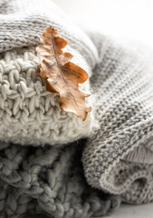 Close-up of a stack of knitted sweaters with autumn leaves.