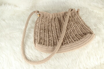 Knitted handmade milky brown bag on furry white blanket. Top view. 