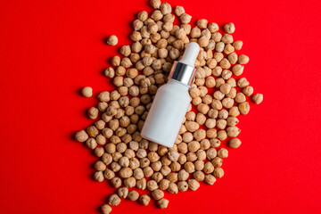Cosmetic product in tube, bottle, lotion or serumon chickpeas source on red background.