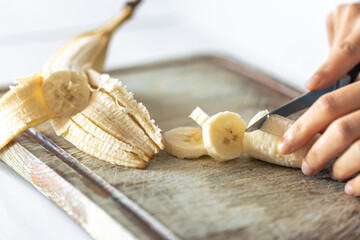 A woman cuts a banana on a cutting board.
