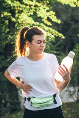 Tired young woman with a bottle of water in the park after a run.