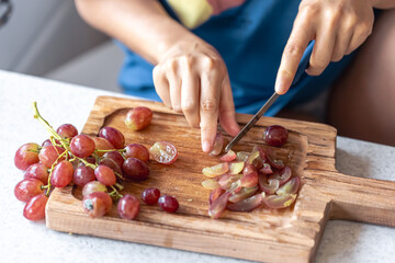 A woman cuts grapes on a cutting board.