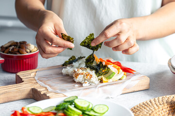 Woman preparing spring rolls in rice paper on kitchen table.
