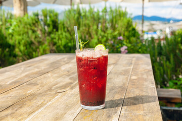 Fresh homemade mulberry ice tea with rosemary and lemon served on wooden table outdoors. summer...