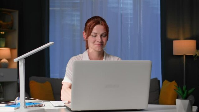 office at home, cute woman working at home at a laptop making notes in notebook while sitting at a table in a cozy room