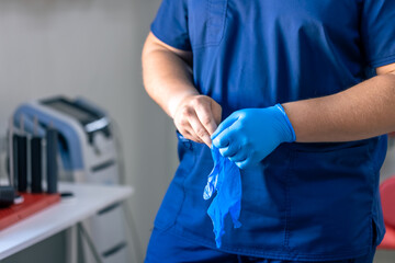A male doctor puts on blue gloves before starting a procedure.
