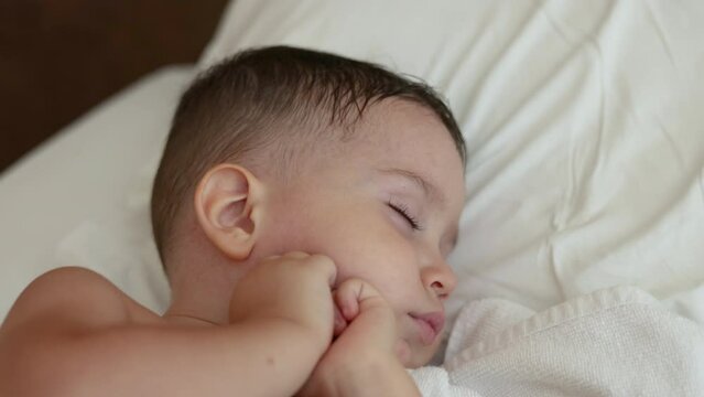 adorable cute baby boy sleeping in bedroom with both hands under cheek chin, sweet face. child kid covered with blanket, close up infant toddler feet. long lashes big lips, adorable portrait.