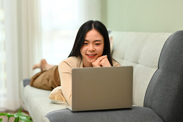 Carefree young woman lying on couch at using laptop. Technology and lifestyle concept