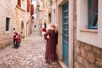 Kobieta w sukni i kapeluszu spacerująca po uliczkach starego miasta Trogir w Chorwacji