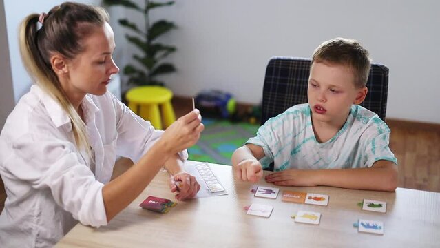 ABA Therapist Leads Therapy Session with Autistic Boy Using Color Cards; Rewards with Tokens; Bright Room with White Walls, Wooden Floor; Fiddle Leaf Fig (Ficus Lyrata) & Toys in the Background