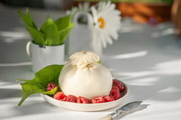 burrata cheese with berries and a cheese knife on the kitchen table in the sun.