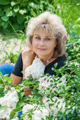 60-year-old woman in the garden. A mature woman enjoys the flowers of a hydrangea grown with her...
