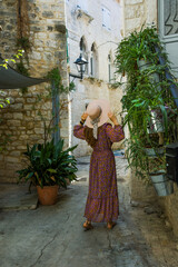 Kobieta w sukni i kapeluszu spacerująca po uliczkach starego miasta © meegi