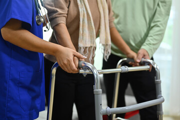 Fototapeta na wymiar Female nurse helping senior woman walking with walker in retirement home. Healthcare service and rehabilitation