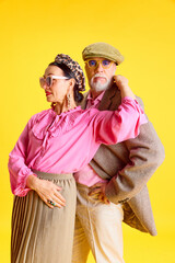 Elegant senior married couple. Beautiful woman and handsome man posing with stylish matching clothes against yellow studio background. Concept of beauty and fashion, relationship, modern style, age