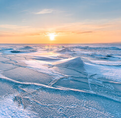 Naklejka premium Winter landscape. A frozen surface of ice with snow intersected by many cracks.