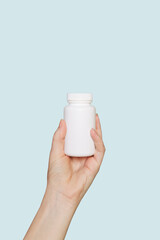 Hand with empty white pill bottle isolated on blue background. Copy space. Bottle with pills. Mockup.