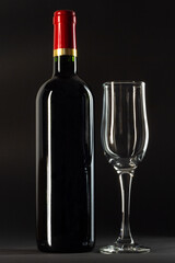 Bottle of red wine and empty wineglass on black background