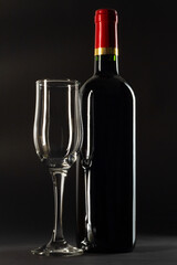 Bottle of red wine and empty wineglass on black background