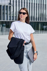 Young businesswoman dressed stylishly walking around the city holding a laptop in her hands