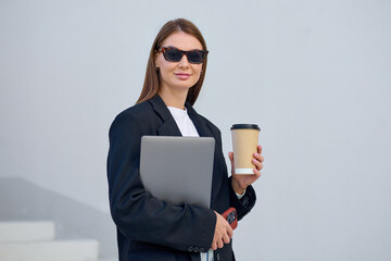 Confident fashionable young woman holding coffee and laptop