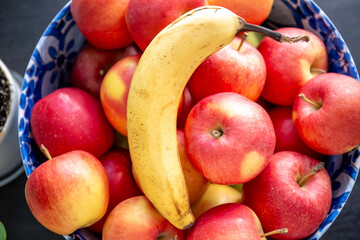 Banana and ripe red apples in a bowl in the kitchen.