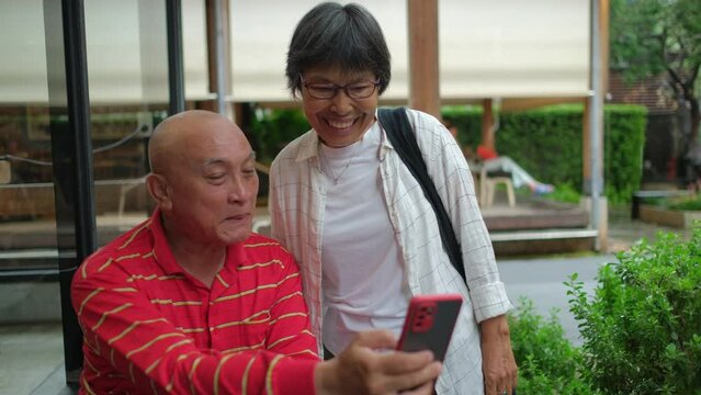 Senior Asian couple enjoys watching clips and pictures of the activities. at mobile phone