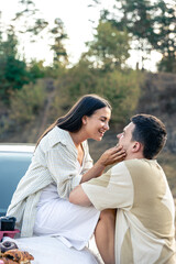 Happy couple enjoy a summer weekend with a car outside the city in a field.