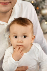 Close-up portrait of a cute little baby in dad's arms near the Christmas tree