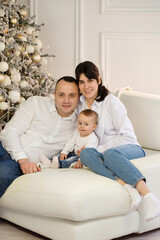 Portrait of a family with a child sitting on a white sofa near a Christmas tree