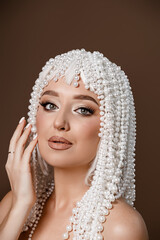 Portrait of a beautiful elegant young woman in a pearl wig posing over beige background. Pretty young lady, studio shot. Beauty. Luxury