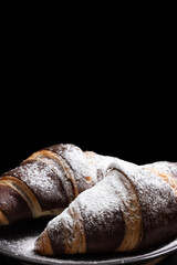 Chocolate croissants with powdered sugar on a black background.