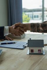 A sales representative shakes hands with a customer and offers a home purchase contract to purchase the current home and a proposed lease for the homeowner. Close-up.