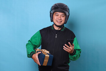 Portrait of Asian online taxi driver wearing helmet, holding box package and smartphone while looking at camera smiling