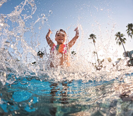 Little girl splashing water in the pool, playing in the water, having fun. Beach resort vacation by sea. Winter or summer seaside holiday.