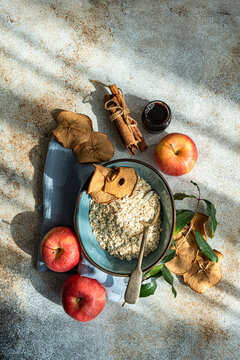 Overhead view of a bowl of Raw oats with fresh and dried apples, jam and cinnamon sticks
