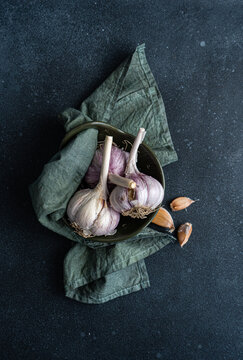 Overhead view of fresh garlic bulbs and cloves in a bowl with a napkin