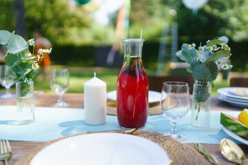 Table setting at a summer garden party. Garden party table with glasses, lemonade, fresh fruits and salad and delicate floral decoration.