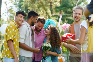 Garden birthday party with surprise. Friends holding birthday gifts and flowers. Family garden gathering during warm autumn day.